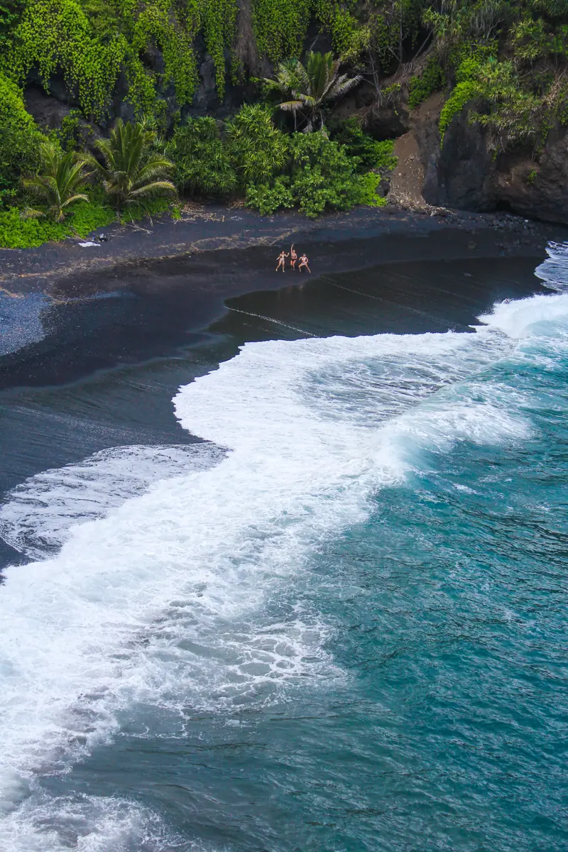 A black sand bay and turquoise surf seen from above