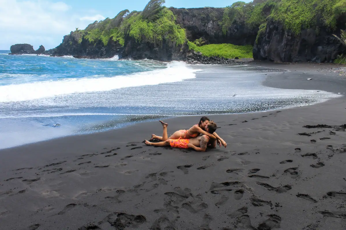A wide view of a black sand cove with two guests on the sand