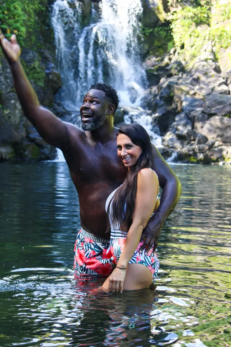 A couple with their arms up in a waterfall pool