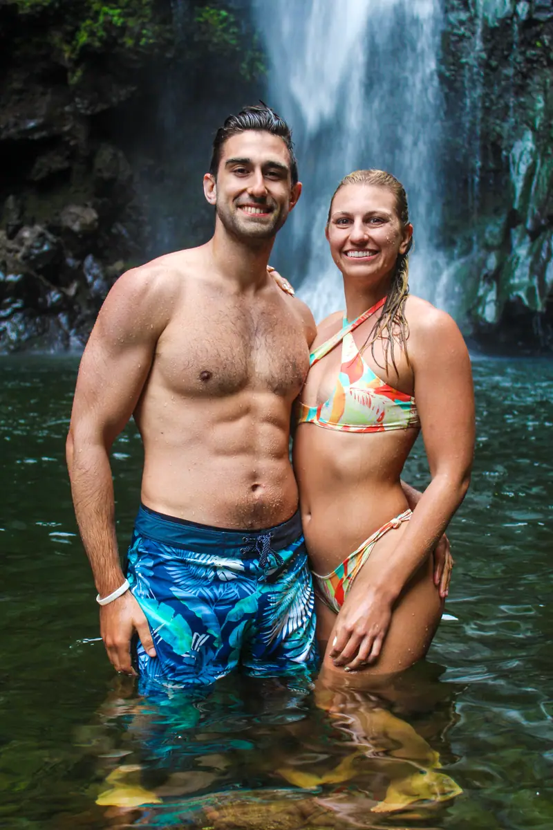 A couple standing waist-deep in a turquoise waterfall pool