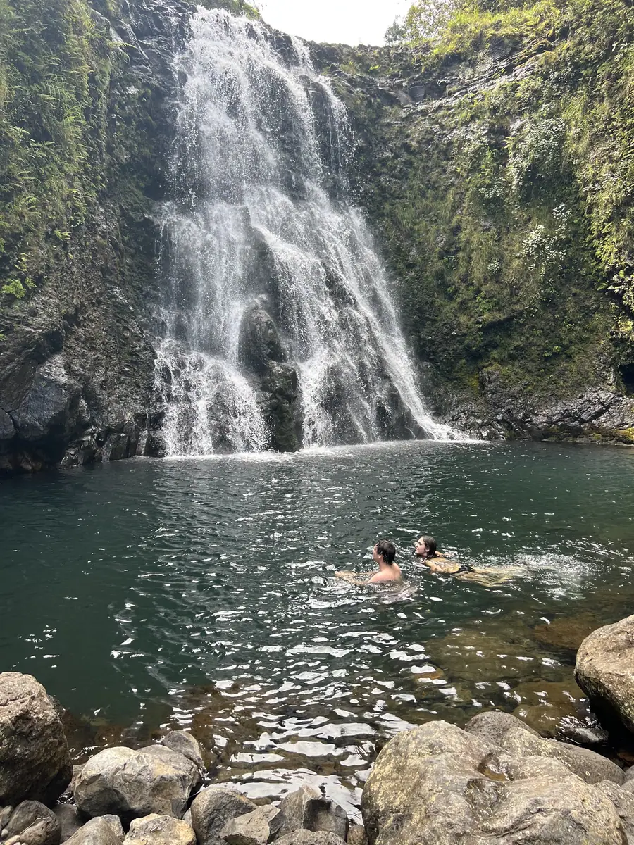 Swimmers dwarfed by the cliff at the base of a waterfall